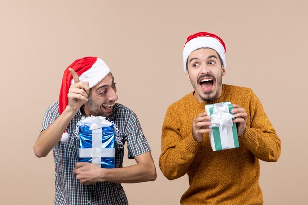 Vista frontal de dos chicos llenos de alegría riendo y sosteniendo regalos de Navidad sobre fondo beige aislado