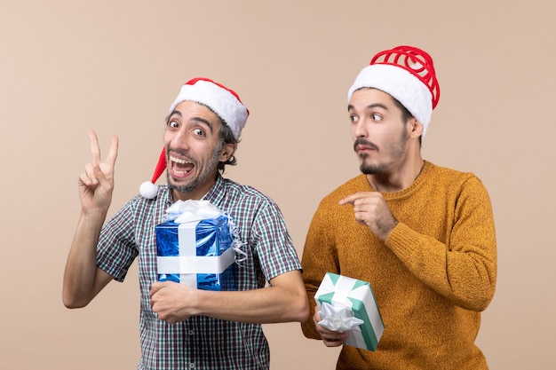 Vista frontal de dos chicos, uno mostrando el signo de la paz de la victoria y el otro confuso sosteniendo regalos de Navidad