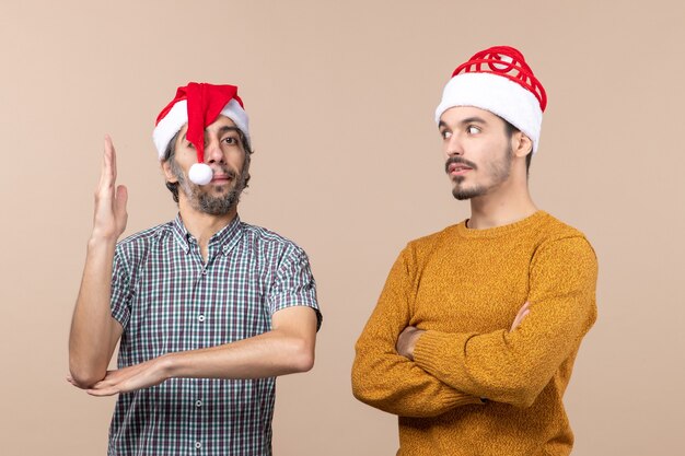 Vista frontal de dos chicos de Navidad, uno levantando la mano y el otro riendo sobre fondo beige aislado