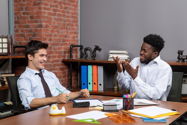 Vista frontal de dos empresarios felices en ropa formal sentados en el escritorio