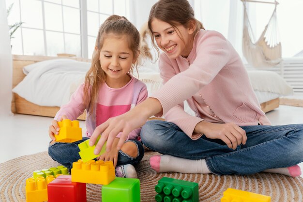 Vista frontal de dos hermanas sonrientes jugando con juguetes en casa