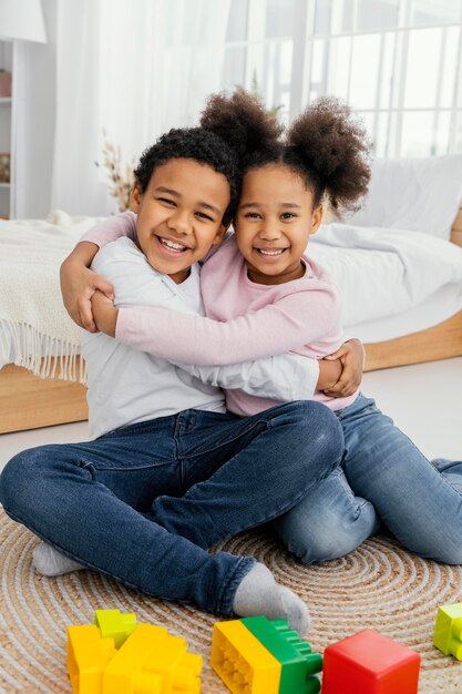 Vista frontal de dos hermanos sonrientes abrazándose en casa