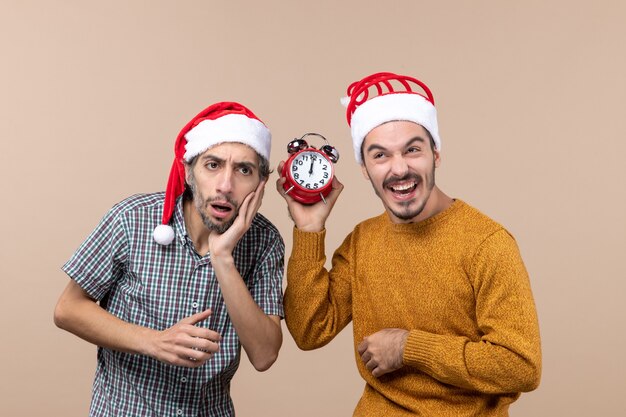 Foto gratuita vista frontal de dos hombres uno confuso y el otro sosteniendo una alarma mientras se ríe reloj sobre fondo beige aislado