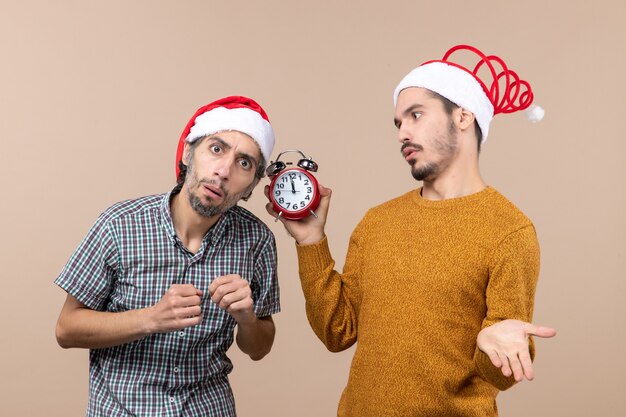 Vista frontal de dos hombres, uno escuchando y el otro sosteniendo un despertador sobre fondo beige aislado