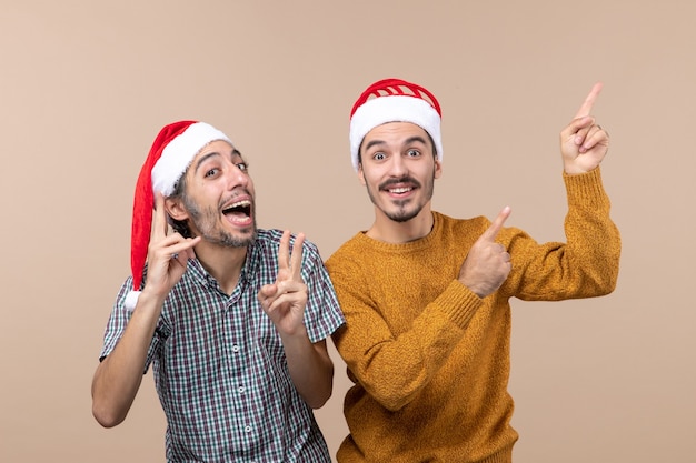 Vista frontal de dos hombres felices con gorro de Papá Noel mostrando algo con gran interés sobre fondo aislado