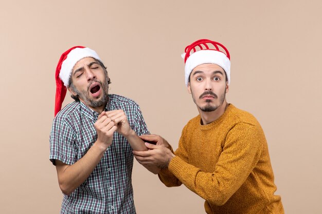 Vista frontal de dos hombres jóvenes, un soñoliento y otro confundido sosteniendo el brazo de los demás sobre fondo beige aislado