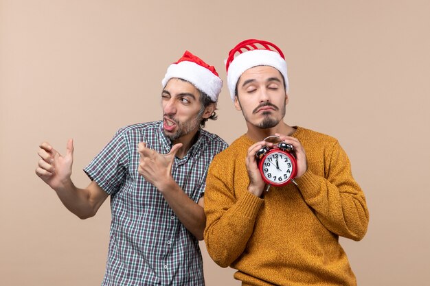 Vista frontal de dos hombres de Navidad, uno con parpadeo y el otro sosteniendo un despertador con los ojos cerrados sobre fondo beige aislado
