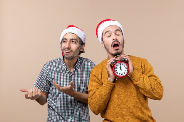 Vista frontal de dos hombres de Navidad uno sosteniendo un reloj despertador con los ojos cerrados sobre fondo beige aislado