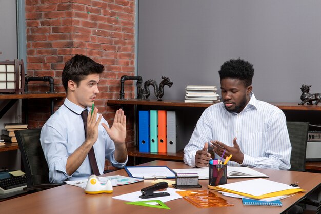 Vista frontal de dos hombres de negocios sentados frente al escritorio y discutir el problema en la oficina