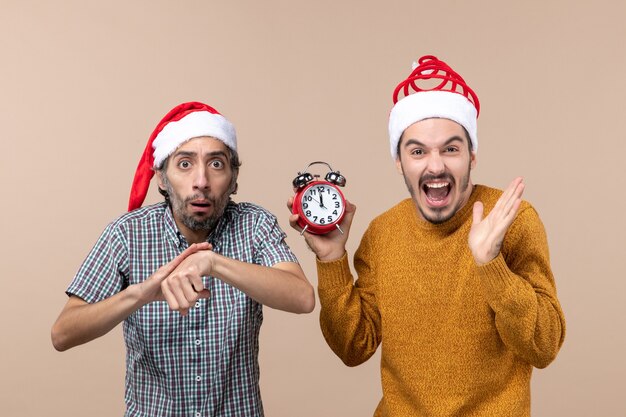 Vista frontal de dos hombres, uno preguntando tiempo y el otro sosteniendo un reloj despertador sobre fondo beige aislado