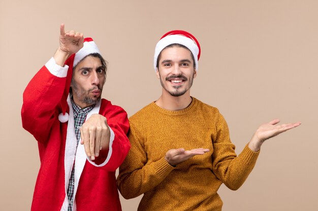 Vista frontal de dos hombres con sombrero de Navidad uno mostrando algo sobre fondo beige aislado