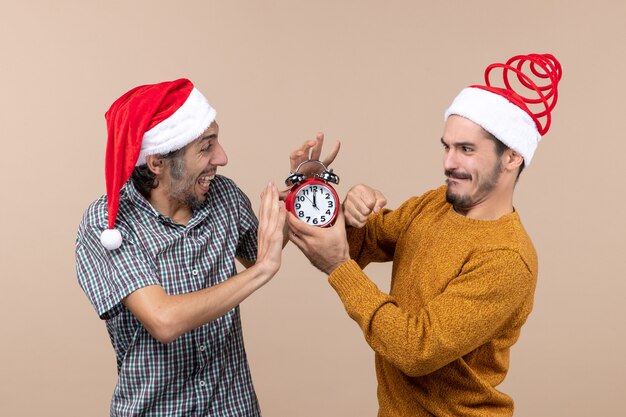 Vista frontal de dos hombres tratando de apagar el despertador sobre fondo beige aislado