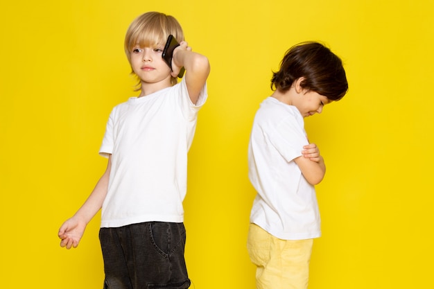 Vista frontal de dos muchachos en camisetas blancas sobre escritorio amarillo
