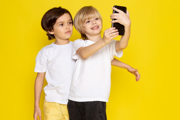 Vista frontal dos muchachos en camisetas blancas tomando selfie en escritorio amarillo