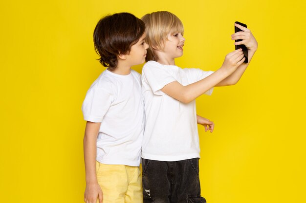 Vista frontal dos muchachos tomando selfie en camisetas blancas sobre piso amarillo