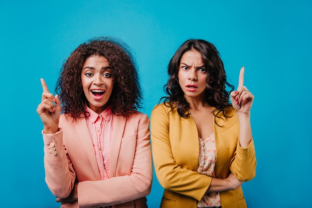 Vista frontal de dos mujeres jóvenes que expresan emociones en la pared azul