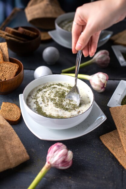 Una vista frontal dovga plato con menta seca dentro de un plato blanco junto con panes de pan huevos flores sobre la mesa sopa líquido caliente sobre el escritorio gris