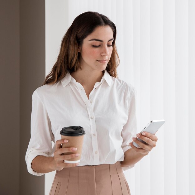 Vista frontal de la elegante empresaria sosteniendo una taza de café y un teléfono inteligente