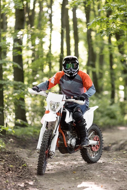 Vista frontal elegante hombre montando moto en el bosque