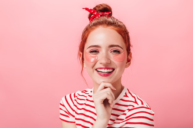 Vista frontal de la elegante mujer jengibre con parches en los ojos. Chica europea con estilo riendo sobre fondo rosa.