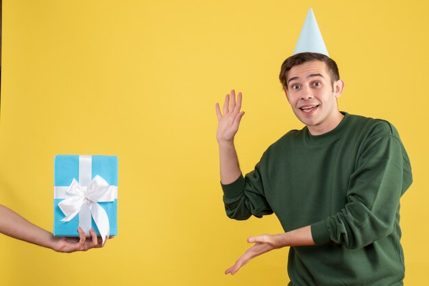 Vista frontal emocionado joven mostrando el regalo en mano humana en amarillo