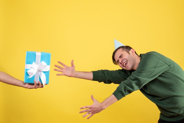 Vista frontal emocionado joven tratando de atrapar el regalo en la mano humana en amarillo