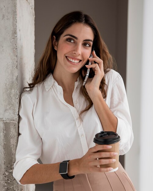 Vista frontal de la empresaria sonriente hablando por teléfono mientras toma un café