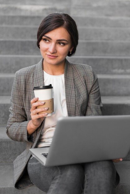Vista frontal de la empresaria tomando café y trabajando en la computadora portátil en pasos