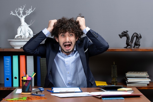 Vista frontal empresario enojado sentado en el escritorio y tirando de su cabello