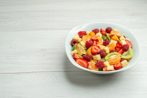 Vista frontal ensalada de frutas kiwis en rodajas, mandarinas, fresas y manzanas en la superficie blanca, color del árbol, suave, madura, foto, dieta, frutal, espacio libre para texto