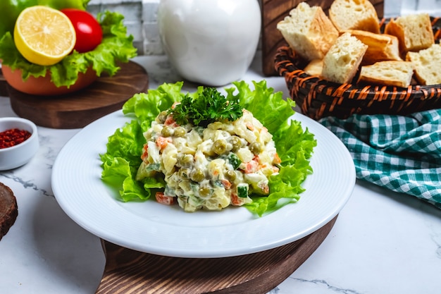 Vista frontal de ensalada de lechuga en un plato con una rodaja de limón y tomate y pan en una cesta