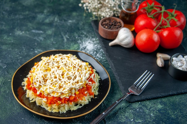 Vista frontal de la ensalada de mimosa dentro del plato con condimentos y tomates rojos sobre una superficie azul oscuro cocina foto cocina comida de cumpleaños comida navideña color