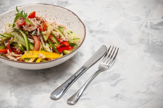 Vista frontal de ensalada de pollo con verduras y cubiertos en superficie blanca manchada