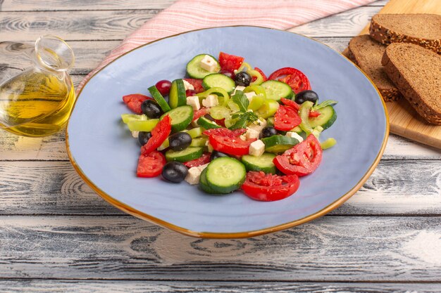 Vista frontal Ensalada de verduras frescas con pepinos en rodajas, tomates, oliva, placa interior con aceite y pan en la superficie gris, comida vegetal, ensalada, color