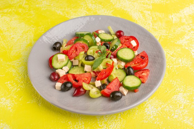 Vista frontal ensalada de verduras frescas con pepinos en rodajas, tomates, oliva, placa interior en el escritorio amarillo ensalada de comida vegetal color de comida