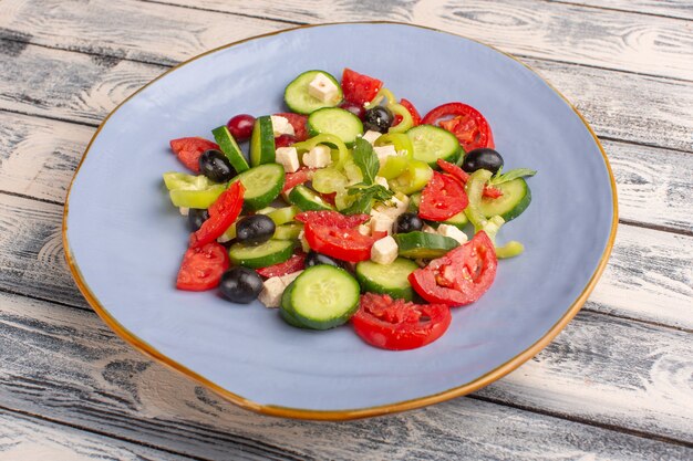 Vista frontal ensalada de verduras frescas con pepinos en rodajas, tomates, oliva, placa interior sobre superficie gris ensalada de comida vegetal color de comida