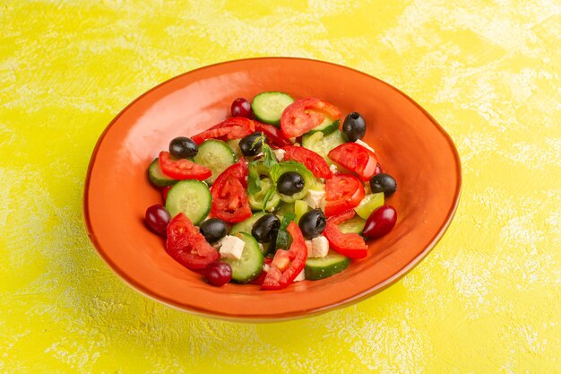 Vista frontal ensalada de verduras frescas con pepinos en rodajas tomates oliva placa interior en la superficie amarilla ensalada de comida vegetal color de comida