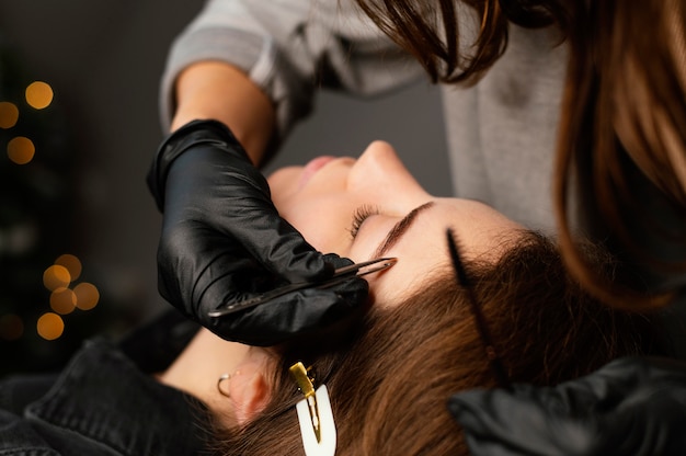 Vista frontal de la especialista femenina haciendo un tratamiento de cejas para mujer