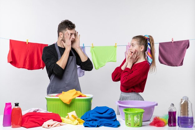Foto gratuita vista frontal de la esposa y el esposo mirándose poniendo las manos en la cara de pie detrás de la mesa cestas de lavandería y lavando cosas en la mesa con una cuerda