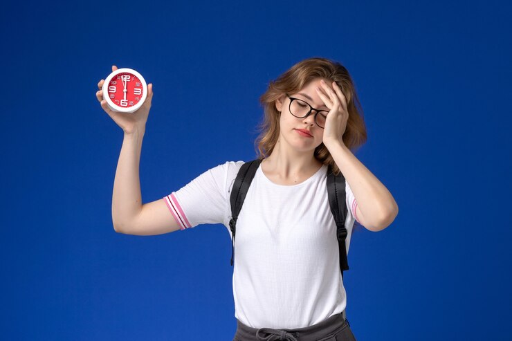 Foto gratuito vista frontal de la estudiante en camisa blanca con mochila y sosteniendo relojes en la pared azul