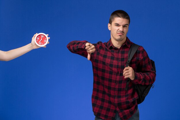 Foto gratuita vista frontal del estudiante en camisa a cuadros roja con mochila en la pared azul