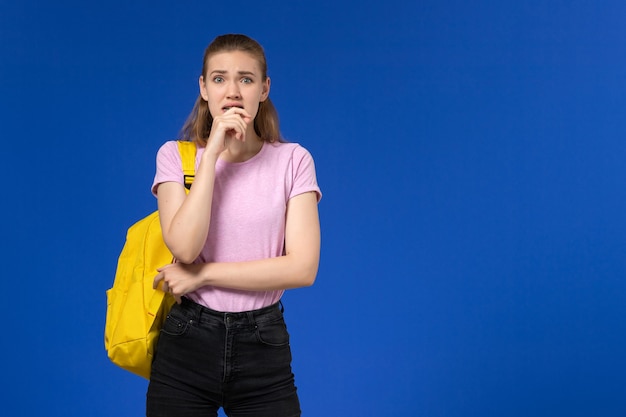 Foto gratuita vista frontal de la estudiante en camiseta rosa con mochila amarilla asustada en la pared azul claro