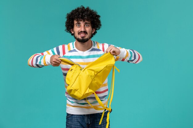 Vista frontal del estudiante con mochila amarilla en la pared azul