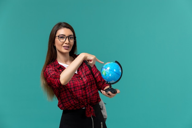 Vista frontal de la estudiante con mochila sosteniendo un pequeño globo en la pared azul claro