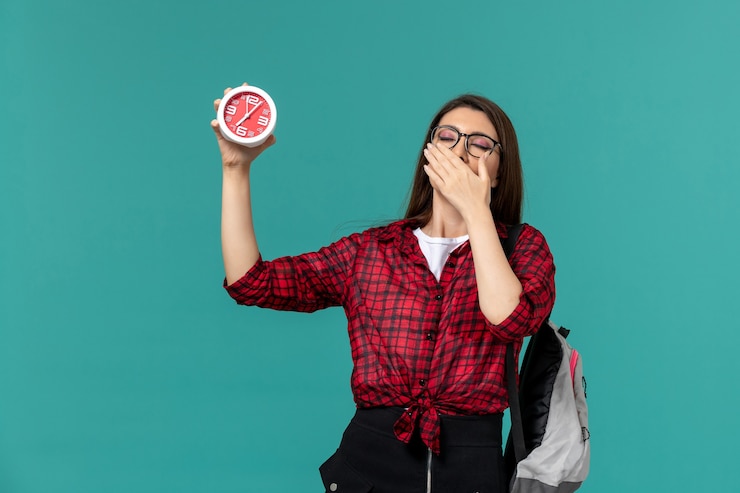 Foto gratuito vista frontal de la estudiante con mochila sosteniendo relojes bostezando en la pared azul