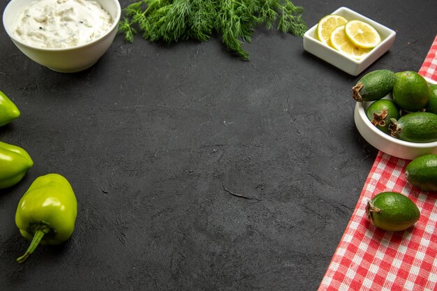 Vista frontal de la feijoa y el limón con pimientos verdes y verduras en la superficie oscura de la harina de frutas y verduras