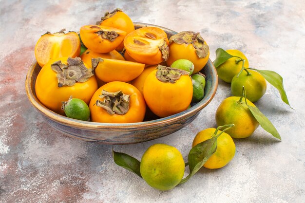 Vista frontal feijoas de caquis frescos en un cuenco y mandarinas sobre fondo desnudo