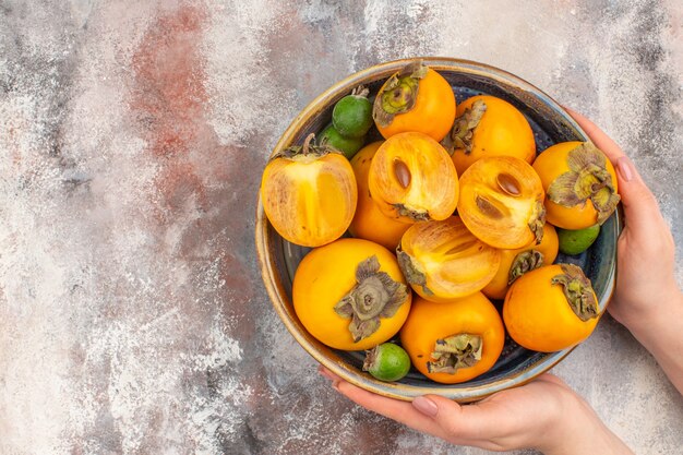 Vista frontal feijoas de caquis frescos en un recipiente en la mano femenina sobre fondo desnudo