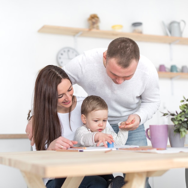 Vista frontal de felices padres con bebé en la cocina