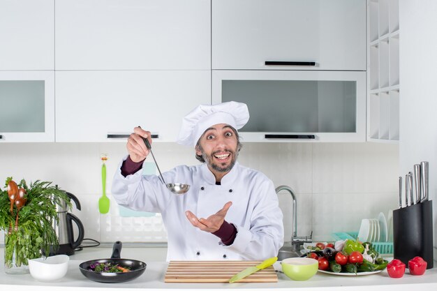 Vista frontal feliz chef masculino en uniforme sosteniendo la pala en la cocina moderna